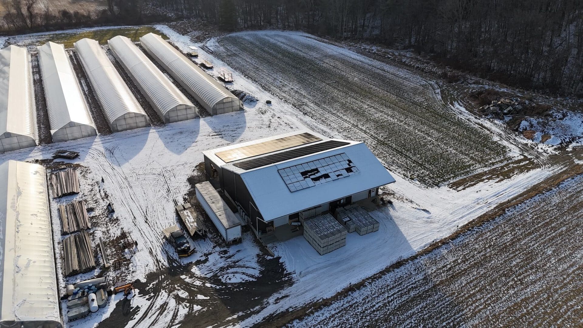 Greenhouse solar panels on a farm with storage and snow-covered fields, promoting sustainable solar energy solutions.