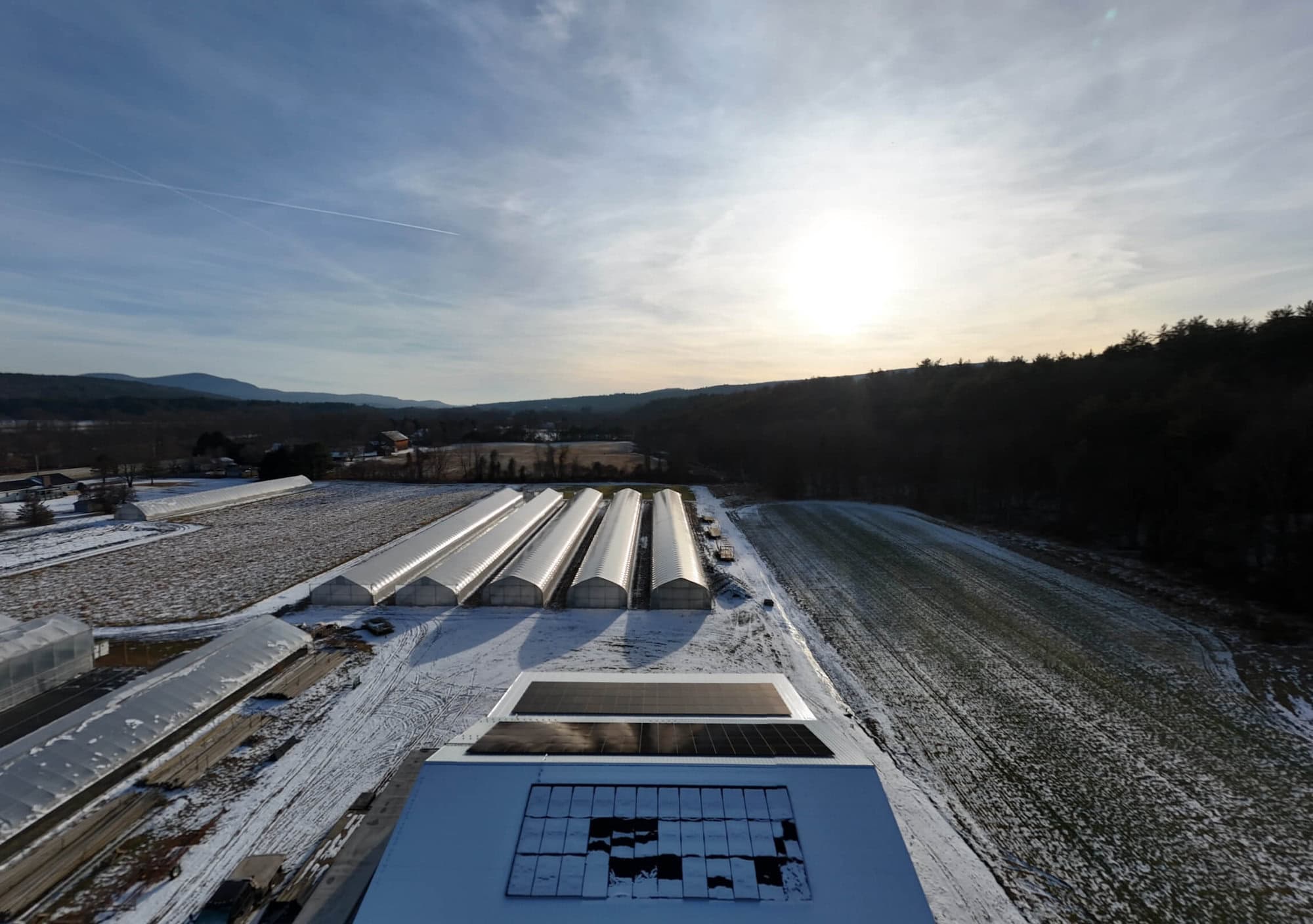 Solar panel array on farm with greenhouses, winter, sunny sky, mountain view.