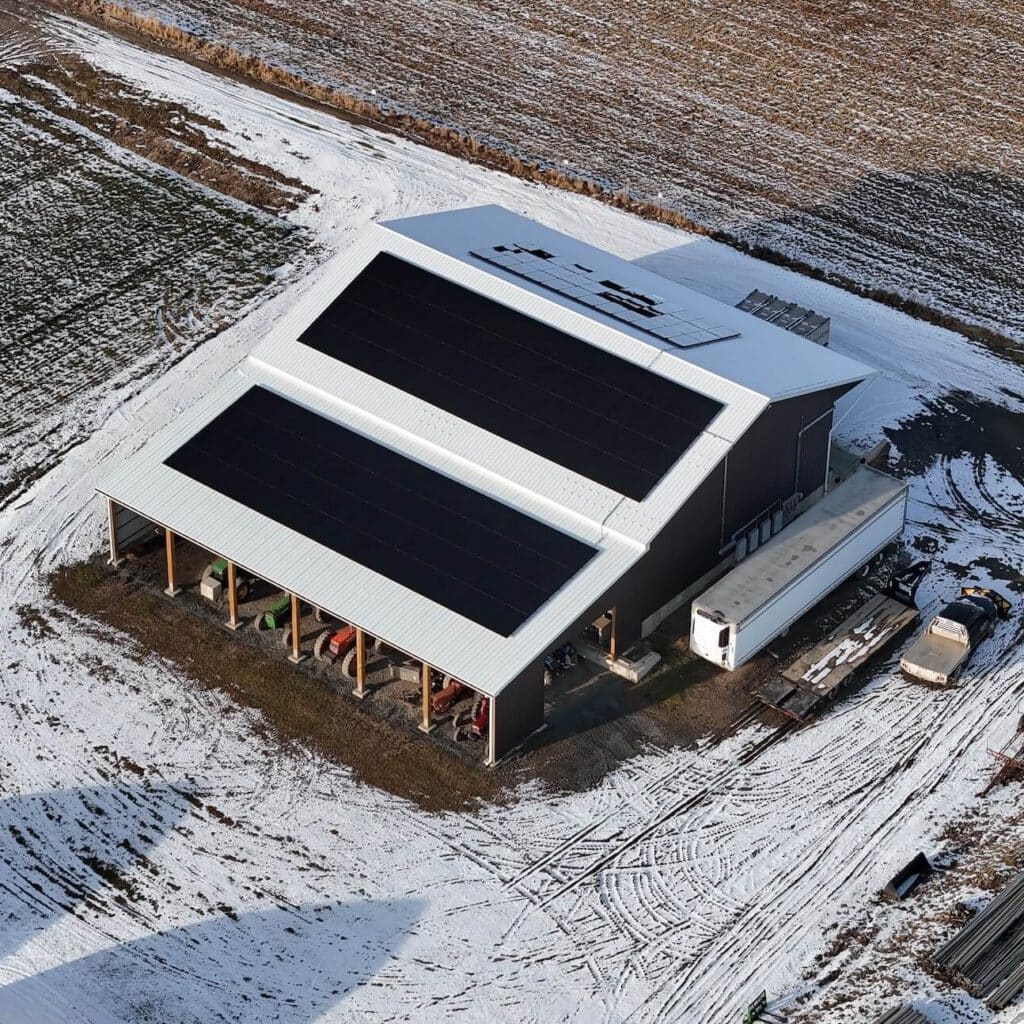 Solar energy farm with black solar panel array on metal roof amid snow-covered farmland.
