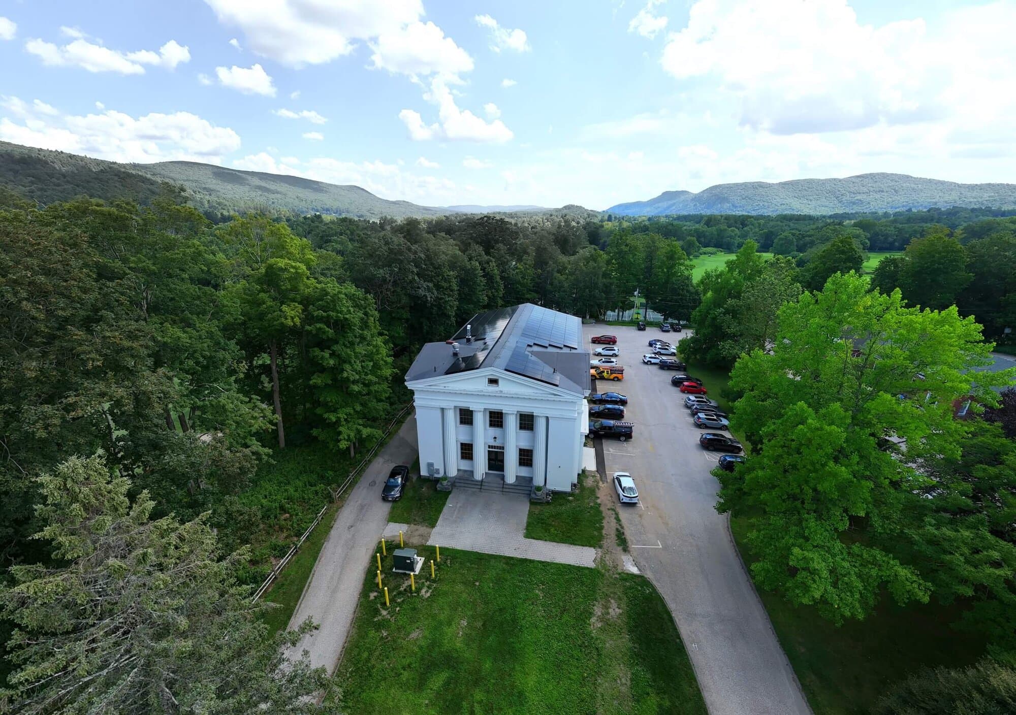 Solar panel array on the roof of a white institutional building in a green landscape.