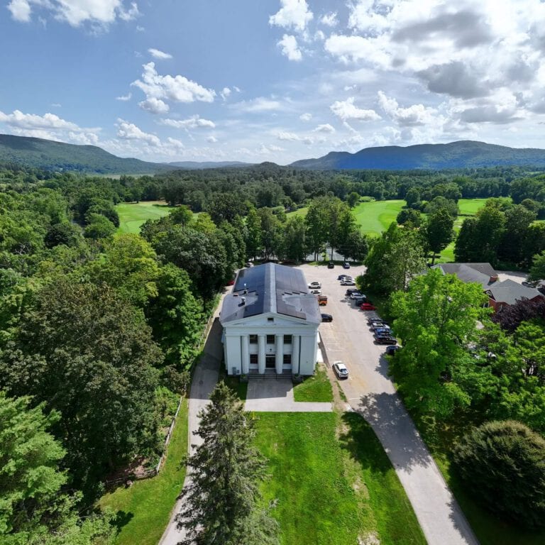 Rich green landscape with mounted solar panels on a historic white building, surrounded by lush trees and mountains, showcasing energy solutions, Valley Solar focus.