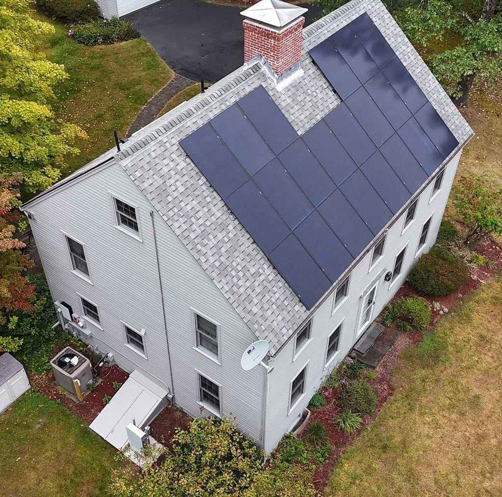 Solar panel installation on residential roof in a lush green backyard.