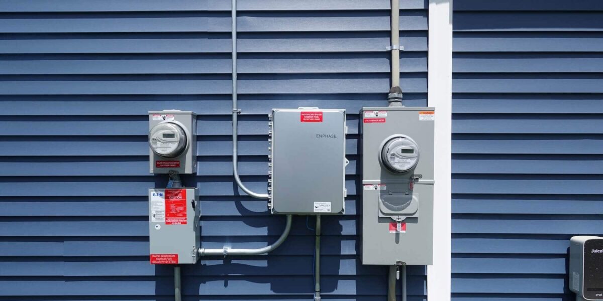 Electrical meters and solar power system components installed on a blue house siding.