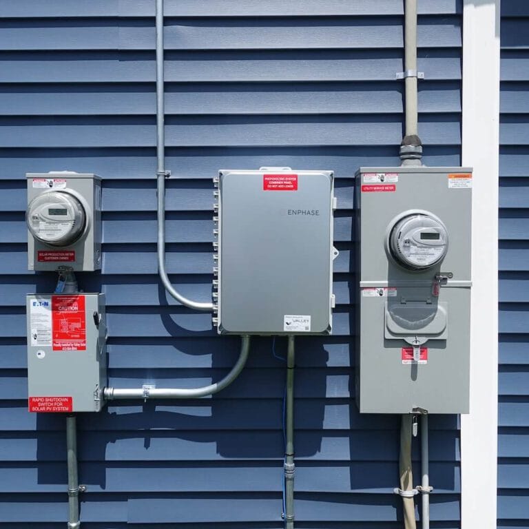 Electrical meters and solar power system components installed on a blue house siding.