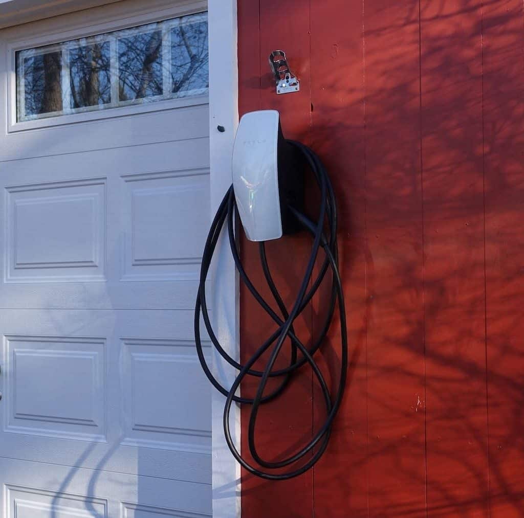 EV charging station with solar power setup on a red wooden garage exterior.