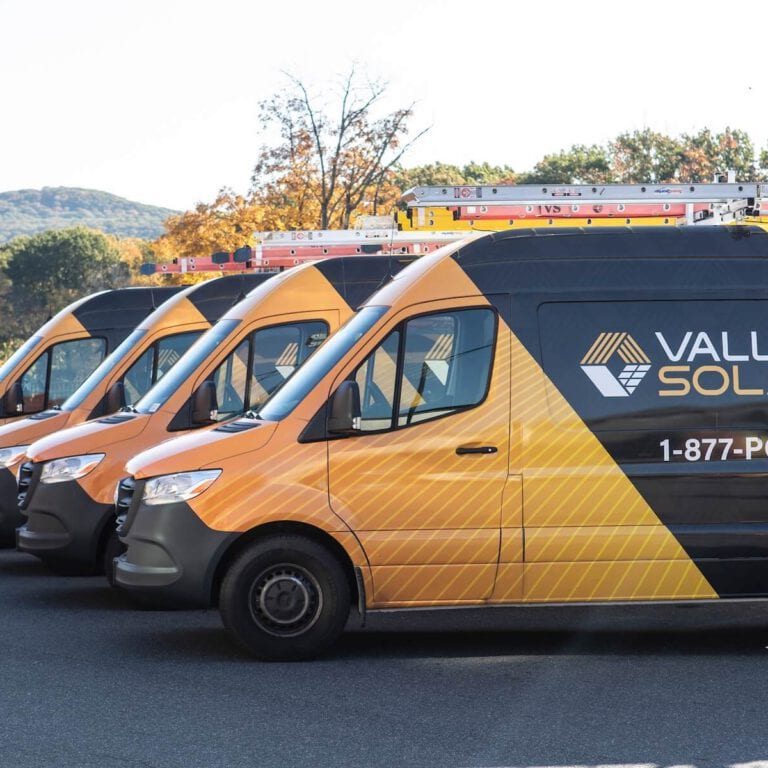 Company branded solar service vans parked outdoors with scenic mountain background.